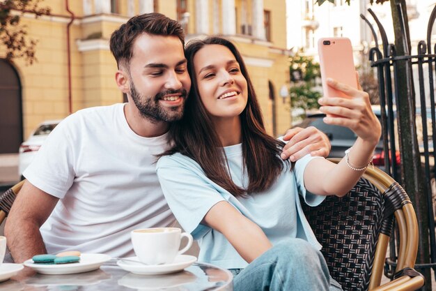 笑顔の美しい女性と彼女のハンサムなボーイフレンドは屋外のベランダカフェでお茶とコーヒーを飲んでいます