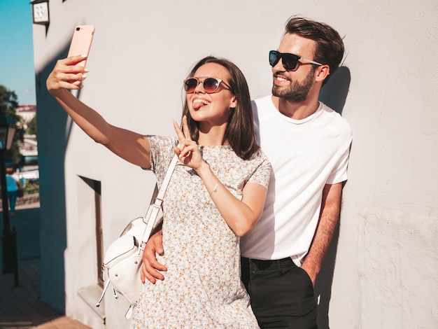 Photo smiling beautiful woman and her handsome boyfriend woman in casual summer clothes happy cheerful family female having fun couple posing on the street background in sunglassestaking selfie photos