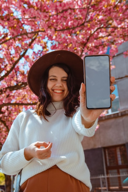 Smiling beautiful woman holding phone with white screen