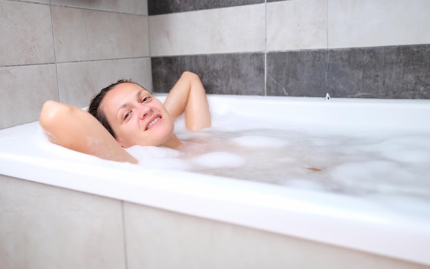 Smiling beautiful woman lies in bath with foam