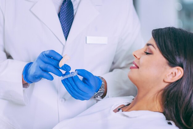 Foto una bella donna sorridente che guarda un dentista maschio che tiene l'apparecchio dentale