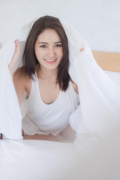 家のベッドの毛布の下に座っている笑顔の美しい女性