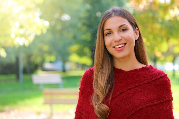 Smiling beautiful woman standing in front of the camera outdoor in autumn or spring season.