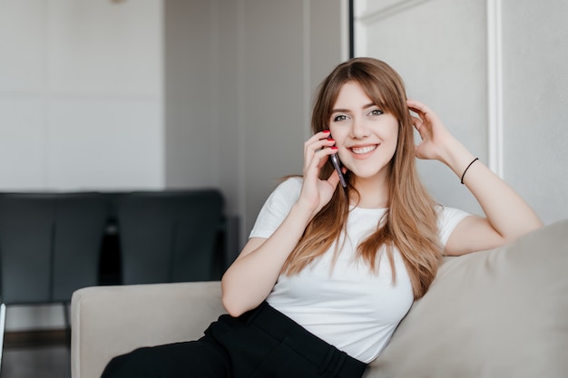 Bella donna sorridente che parla sul telefono che si siede su uno strato a casa