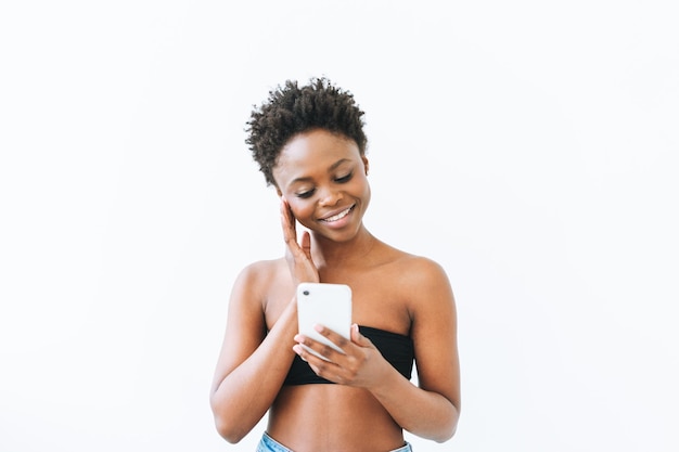 휴대 전화를 사용하여 검은 상단에 웃는 아름다운 젊은 아프리카계 미국인 여자