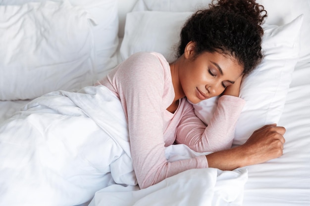 Foto sorridente bella giovane donna africana sdraiata a letto la mattina, dormendo