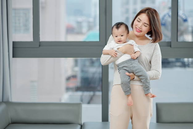 Smiling beautiful young Asian woman carrying her little daughter