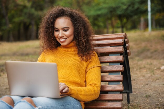 smiling beautiful young curly woman sit in park outdoors using laptop computer.