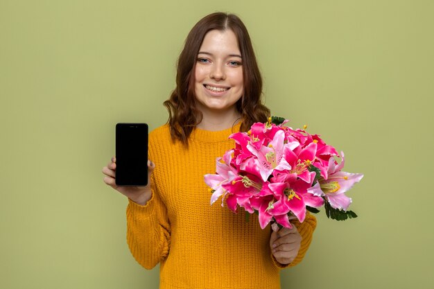 Smiling beautiful young girl holding bouquet with phone