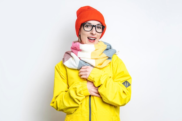 Smiling beautiful young woman in a hat, in a yellow jacket on a light background.