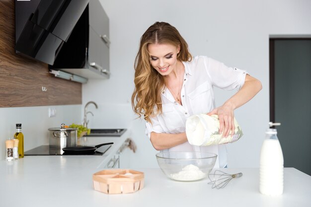 笑顔の美しい若い女性が生地を準備し、キッチンで白い小麦粉を使う