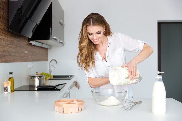 Smiling beautiful young woman preparing dough and using white flour on the kitchen