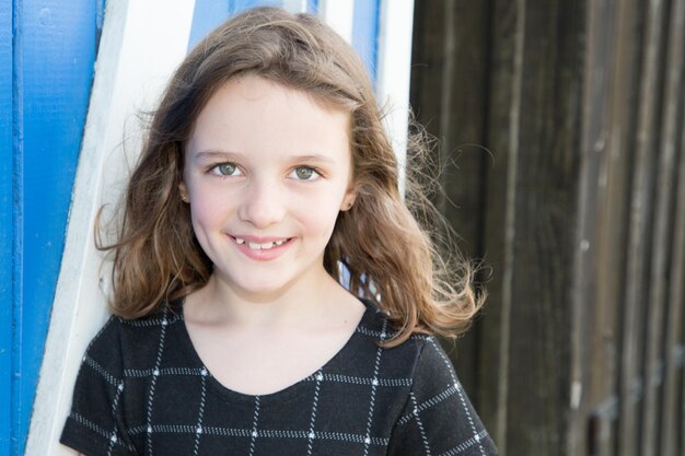 Smiling beauty child girl against wood hut outdoors