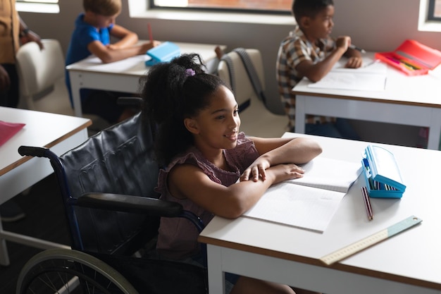 사진 교실 의 책상 에서 체어 에 앉아 있는 미소 짓는 두 인종 의 초등학교 소녀