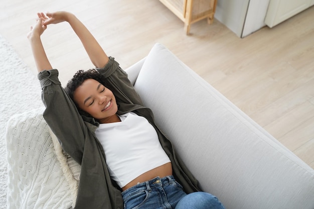 Smiling biracial girl rest lying on couch at home stretching body waking up after sleep Wellness