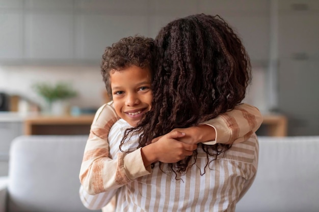 Photo smiling black boy with curly hair embracing his loving mother at home