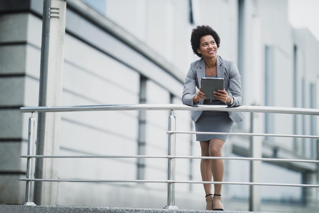 A smiling black business woman working on a digital tablet in
front a corporate building.