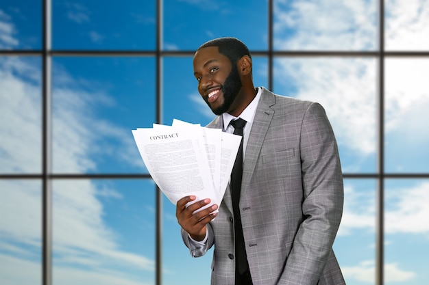Smiling black businessman holds contracts.