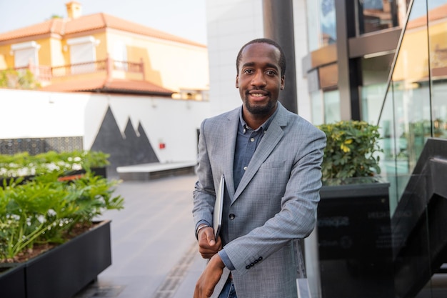 Photo smiling black businessman is elegantly dressed and is holding his laptop. confident and happy business manager. established millennial person