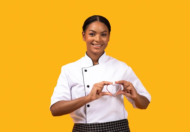 Smiling black female chef holding heartshaped cookie mold near chest