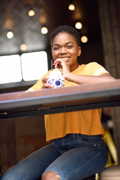 Smiling black girl with very short hair drinking a cocktail in an urban cafe.