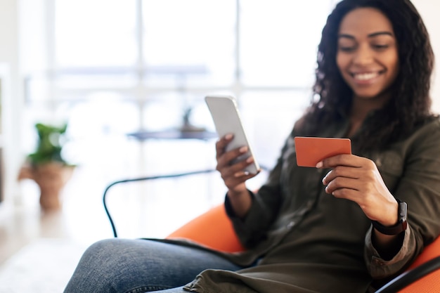 Smiling black lady using phone and credit card at home