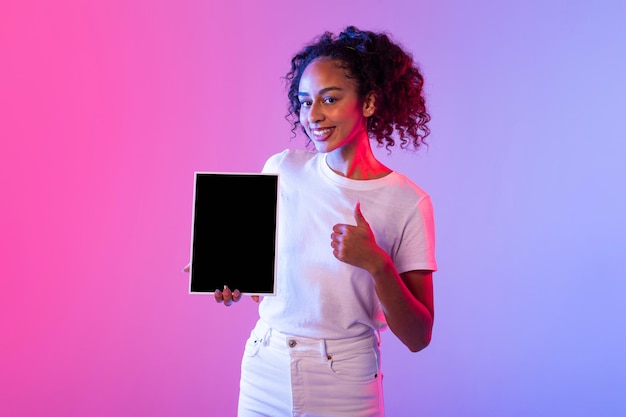 Smiling black lady with tablet giving thumbs up on colorful background