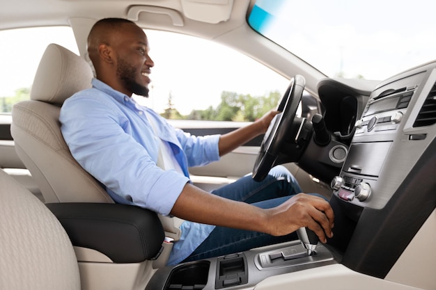 Smiling black man driving new car in city