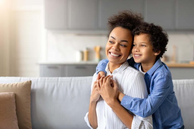 Smiling black mother and son enjoying happy embrace at home looking at free space