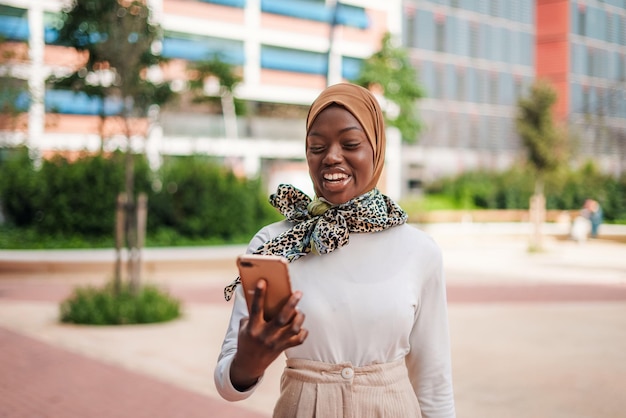 Photo smiling black muslim lady checking message on smartphone