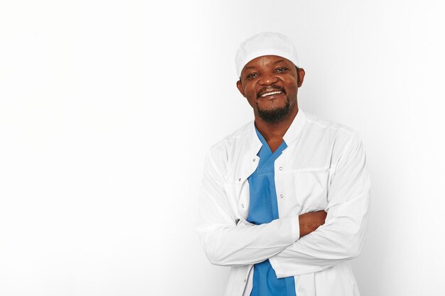 Smiling black surgeon doctor bearded man in white coat and cap with crossed arms isolated on white