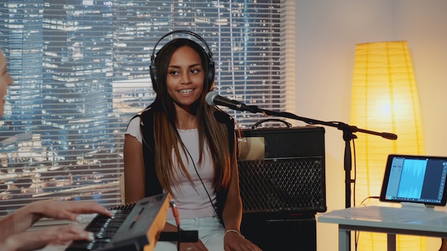 Smiling black vocalist in headphone singing song into microphone in home recording studio