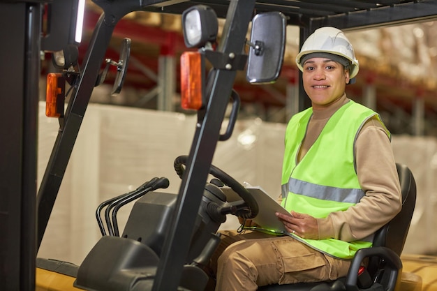 Smiling black woman operating forklift truck in warehouse