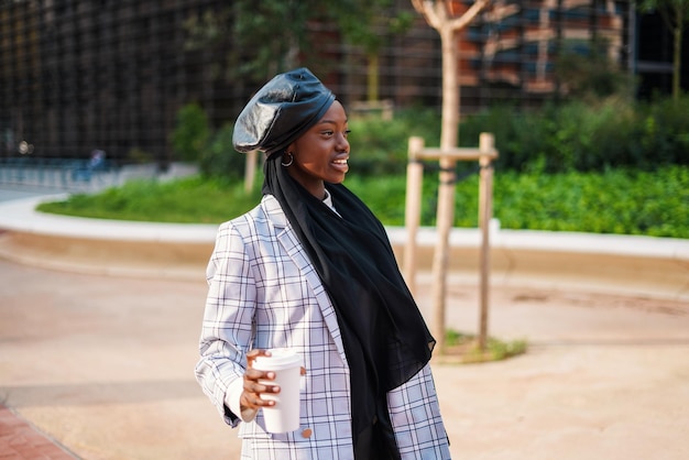 Smiling black woman in scarf and with coffee in city park