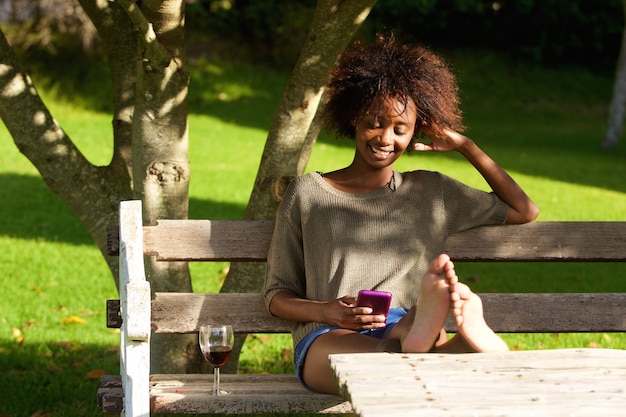 Smiling black woman sitting in park with mobile phone