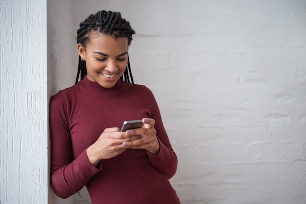 Donna sorridente nera che tenta su smartphone da parete