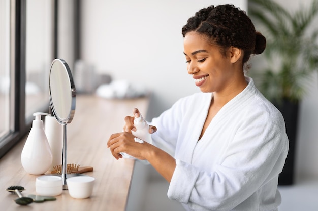 Smiling black woman using moisturising cream for hands at home