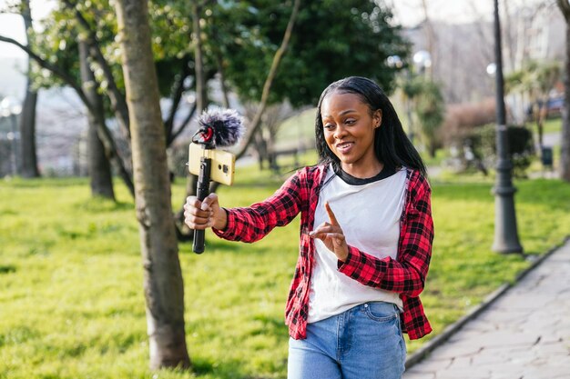 Smiling black woman vlogging outdoors with a phone and mic