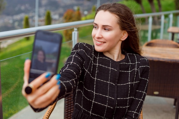 Smiling blogger girl is taking selfie with back camera of smartphone on nature view background