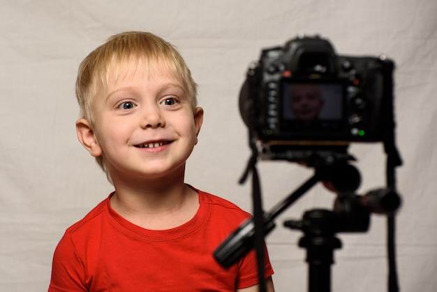 Smiling blond boy in front of the camera lens. Little video blogger. Home studio