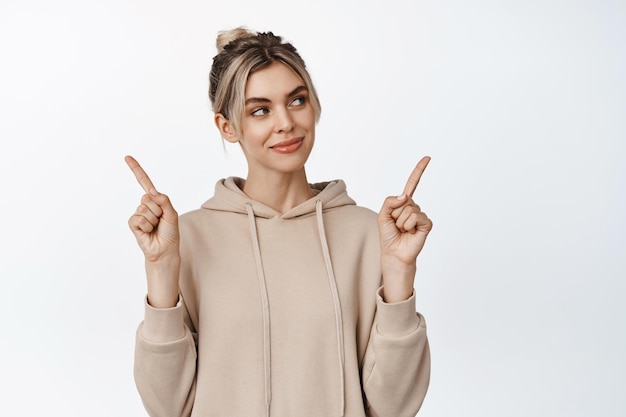 Smiling blond girl makes choice between two variants looking at one option with pleased determined face stands against white background