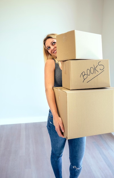 Photo smiling blond woman carrying three moving boxes