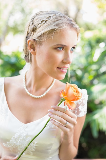 Smiling blonde bride in pearl necklace holding orange rose
