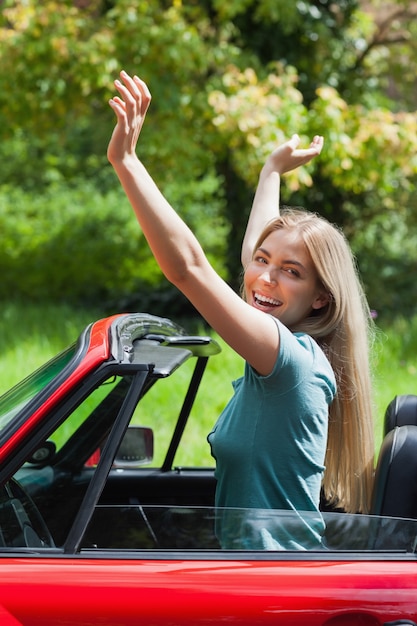 Foto bionda sorridente che gode del suo cabriolet rosso