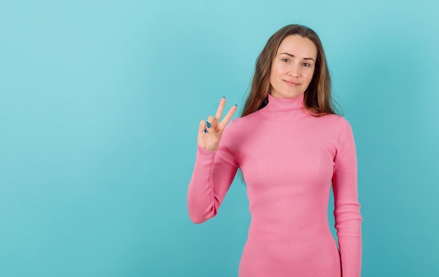 Smiling blonde girl is showing victory gesture on blue background