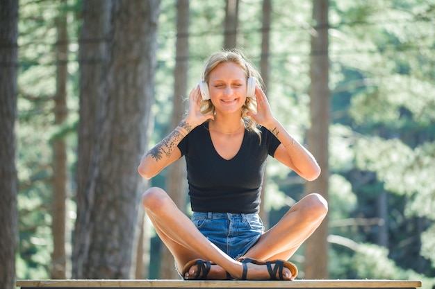 Smiling blonde girl is wishing while listening music on headphone on nature background