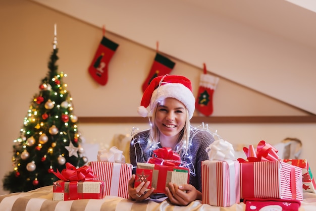 Smiling blonde girl lying on bed surrounded by gifts.