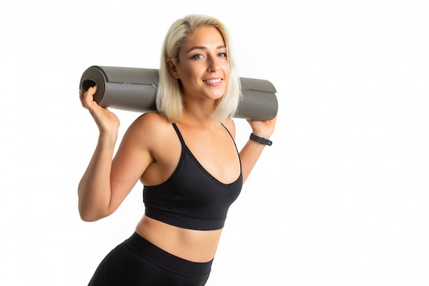 Smiling blonde girl in uniform holds a mat behind her back on white