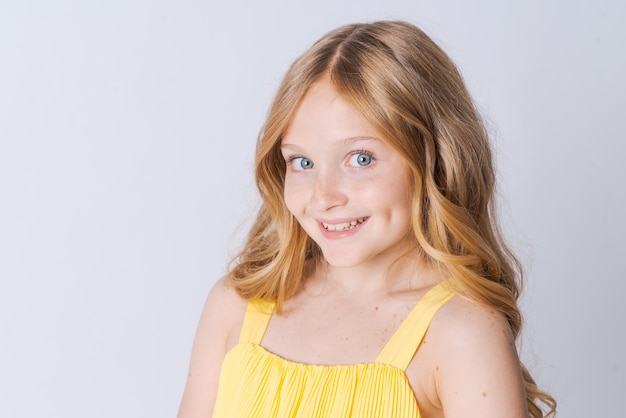 Smiling blonde girl in yellow summer suit posing isolated on light gray