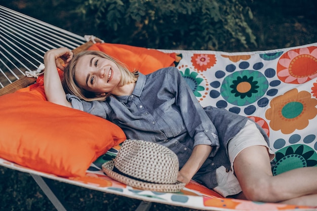 Фото Улыбающаяся блондинка-хипстер отдыхает в гамаке в парке летним отдыхом с женщиной, лежащей на открытом воздухе, концепция кемпинга